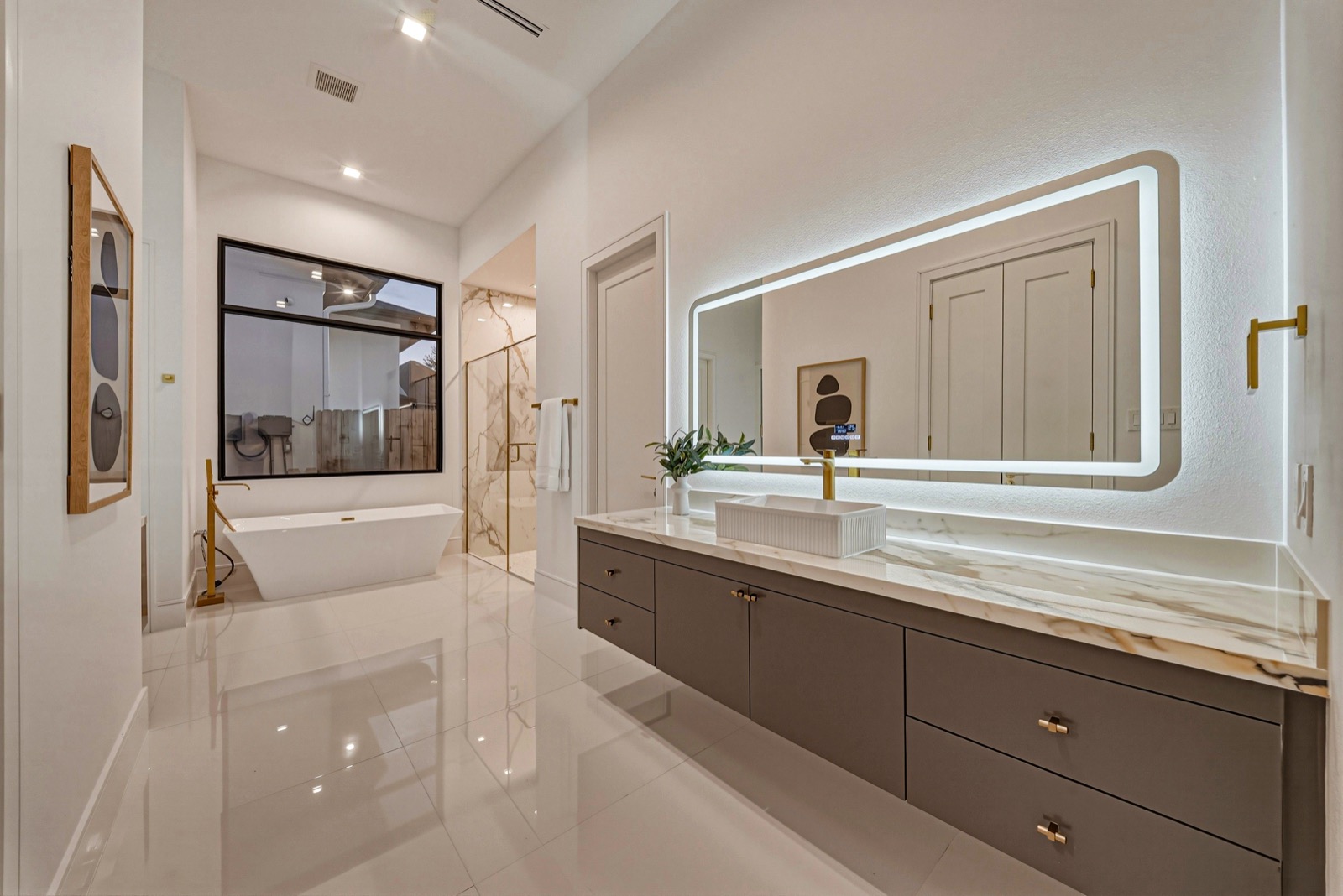 Contemporary bathroom with marble surfaces and a long illuminated mirror