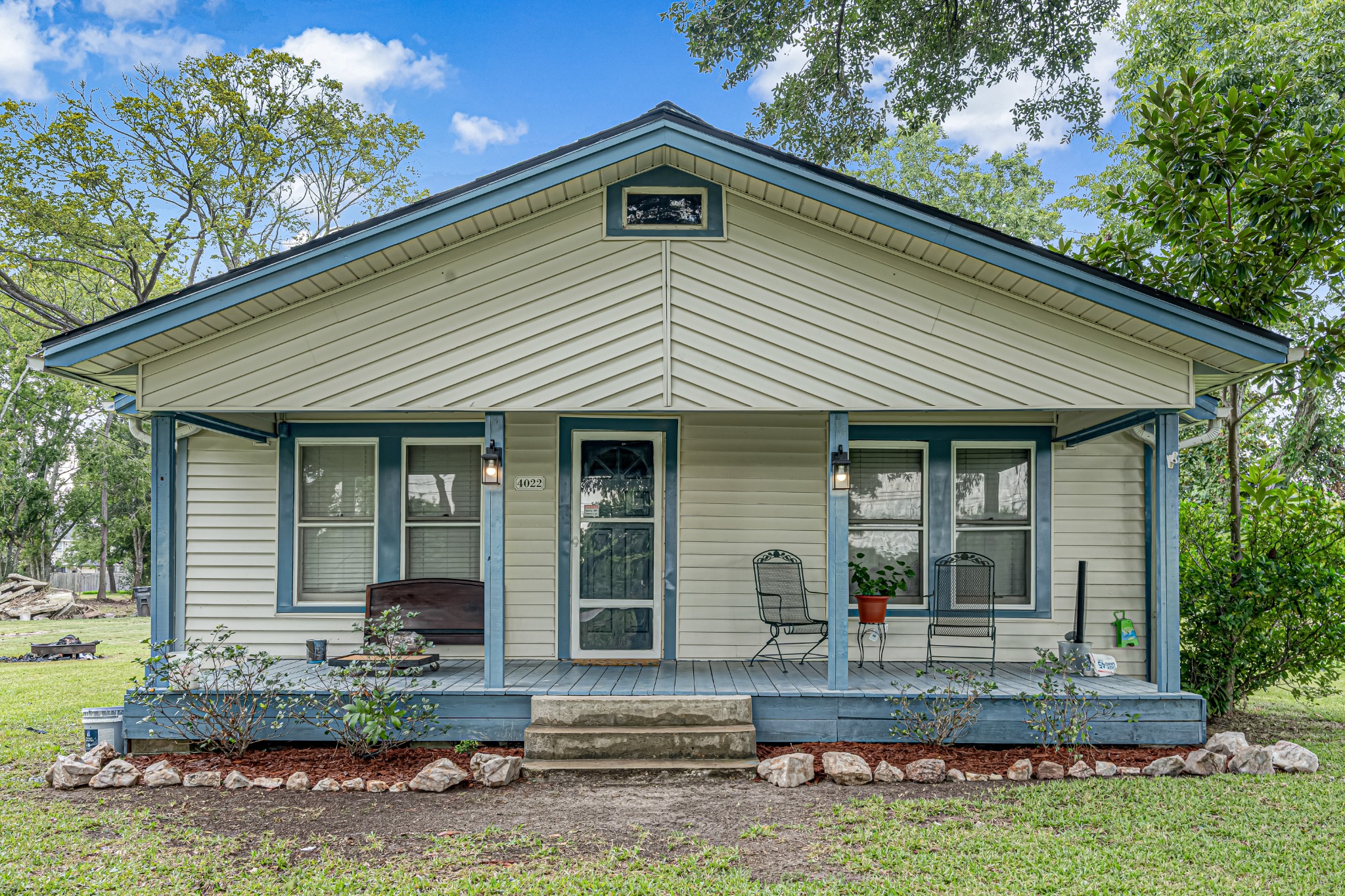 Single-story cottage with a broad front porch beneath mature trees