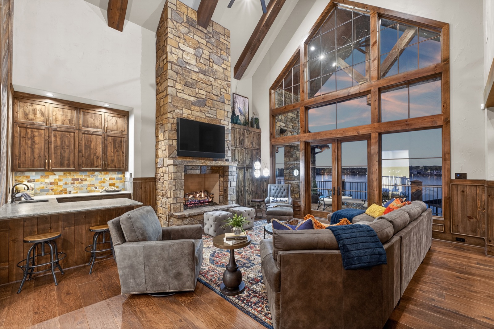 Great room with stone fireplace, exposed beams, and tall windows