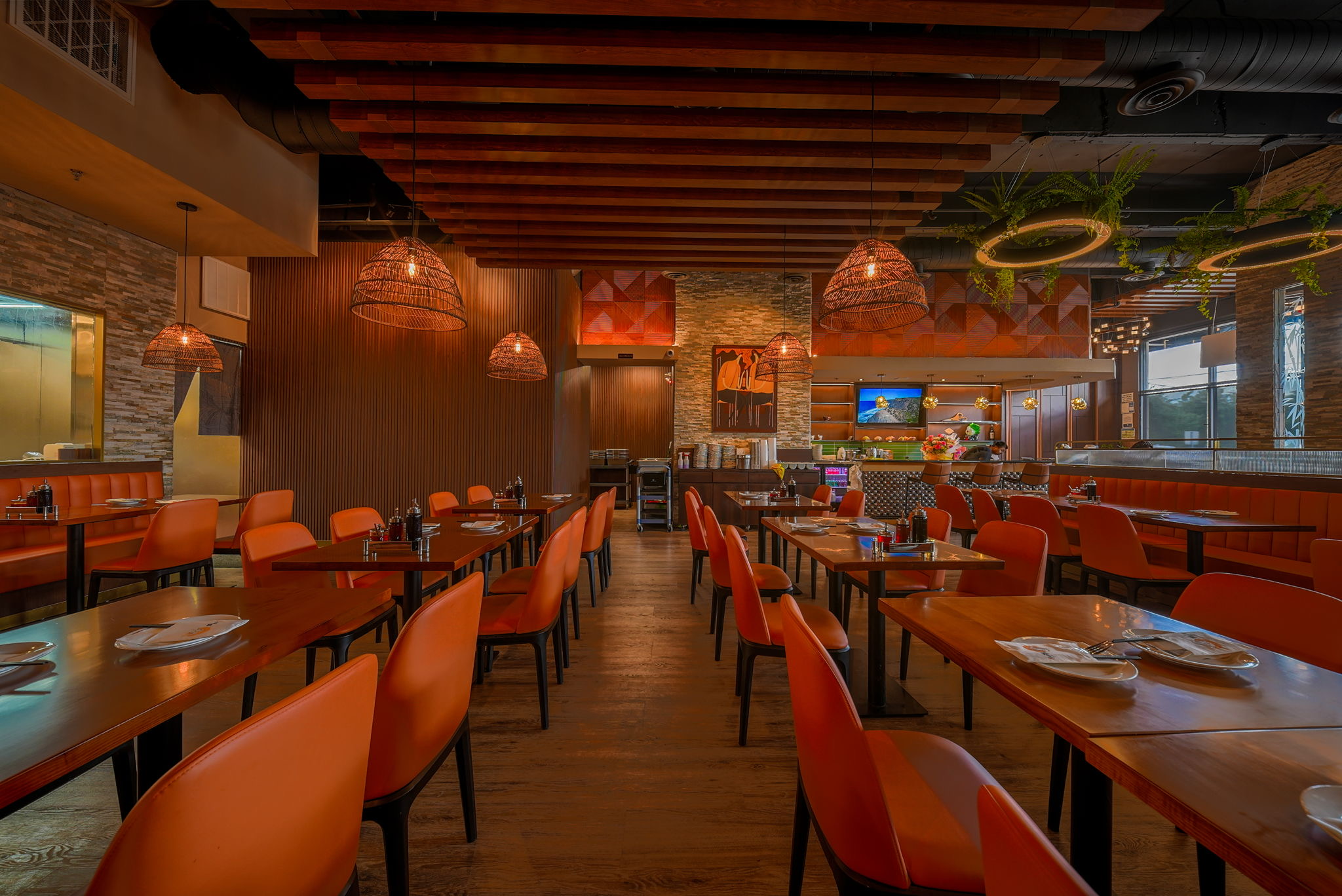Warm restaurant dining room with orange seating, wood beams, and hanging lights