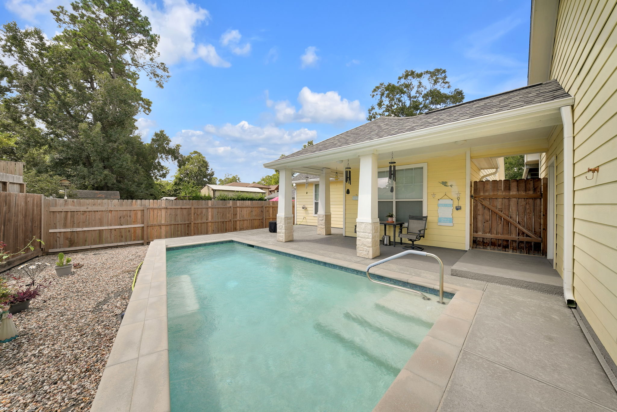 Backyard swimming pool beside a covered porch and pale stone patio