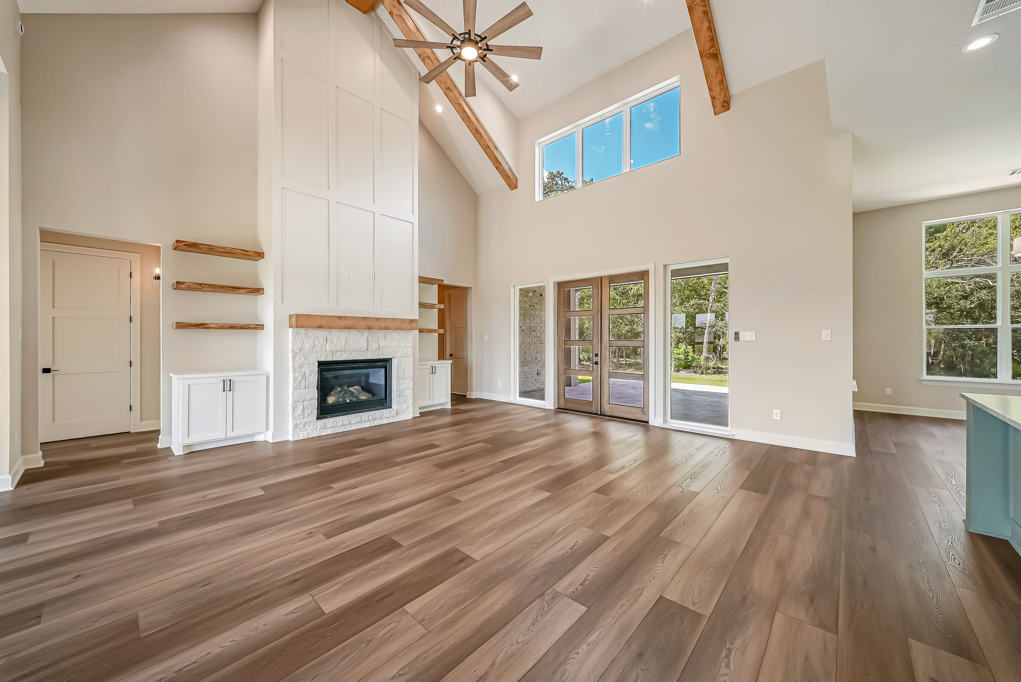 Double-height living room with wood beams, fireplace, and tall windows