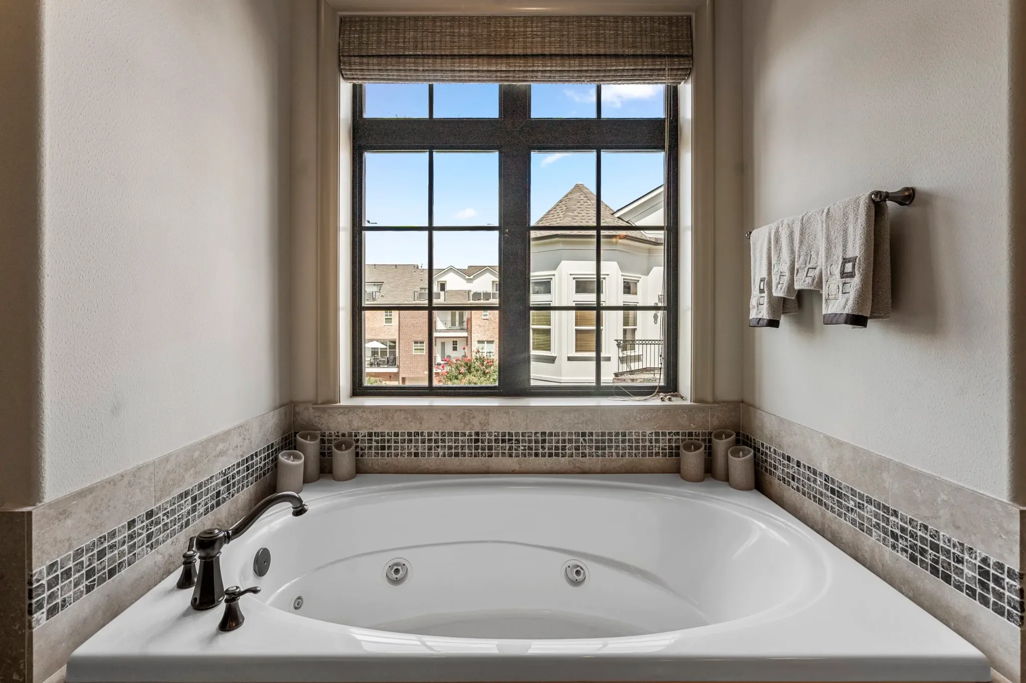 White soaking tub beneath a large window with a neighborhood view