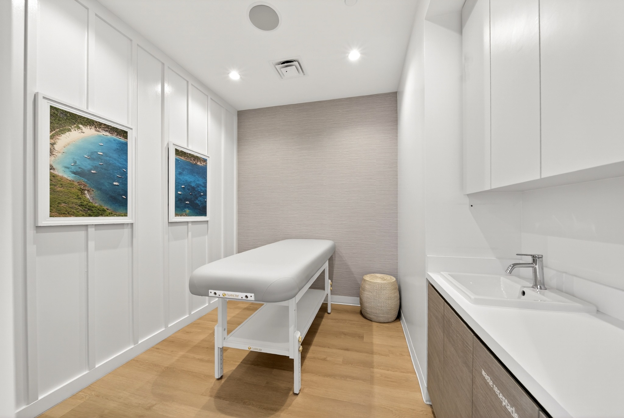 Treatment room with a bed, sink, and coastal photographs